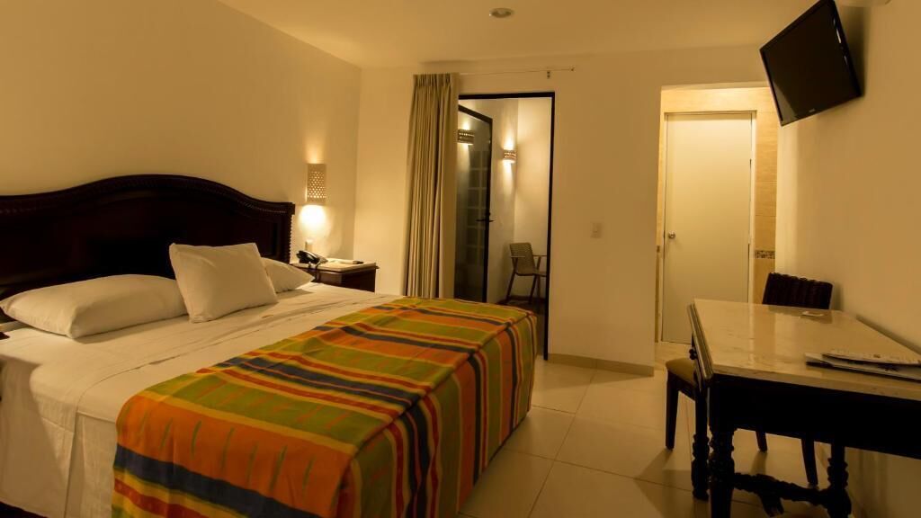 Une chambre d’hôtel comprenant un lit, une table de chevet, une lampe et un bureau avec une chaise.