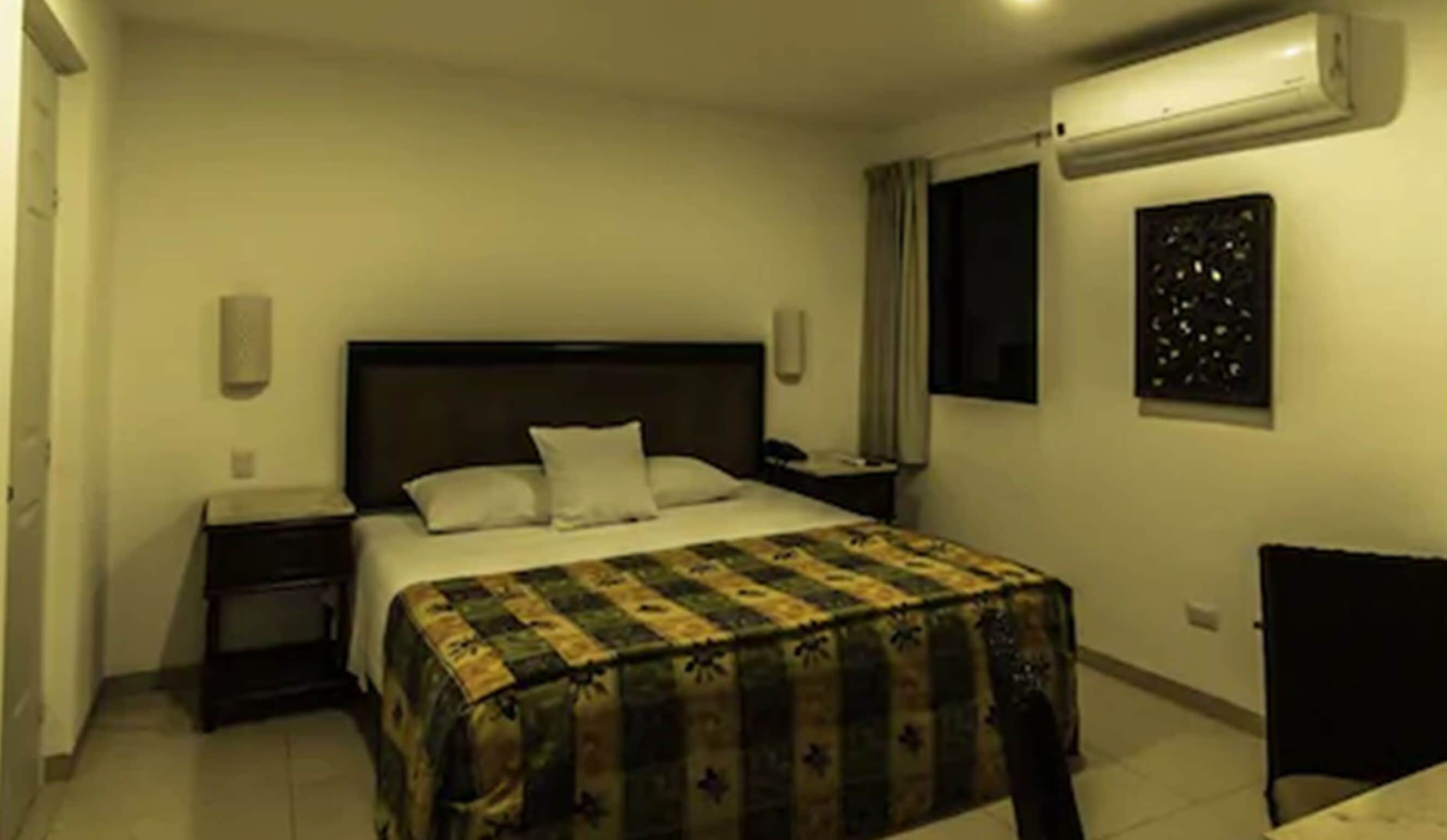 Ein Hotelzimmer mit Bett, Nachttisch, Sessel, Fenster und Klimaanlage.