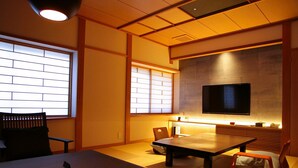 A traditional Japanese-style room with tatami flooring, a low table, a sofa, and a television mounted on the wall. - Kinosaki Onsen Ichidaya (Toyooka)
