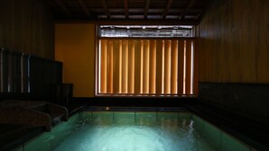A traditional Japanese onsen with a wooden interior, a stone bath, and a view through shoji screens. - Kinosaki Onsen Ichidaya (Toyooka)