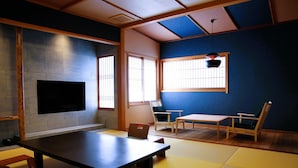 A traditional Japanese room with tatami flooring, a low table, a sofa, and a TV mounted on the wall. - Kinosaki Onsen Ichidaya (Toyooka)