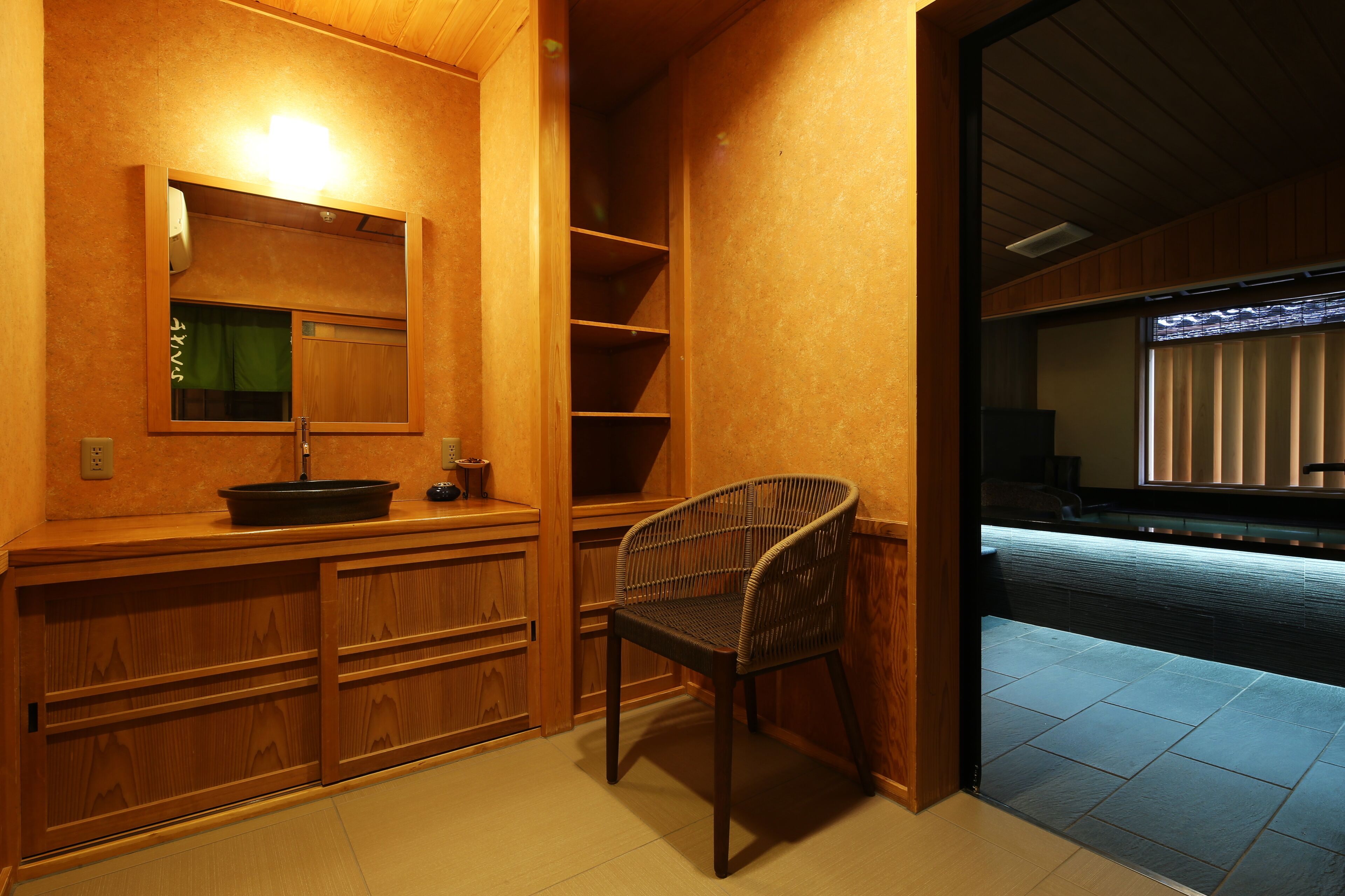 Un baño con tocador de madera, un espejo y una silla de mimbre.