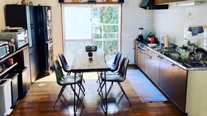 A compact kitchen with a dining table, chairs, and a view through a sliding door. - Life is a Journey - Hostel (Yomitan)