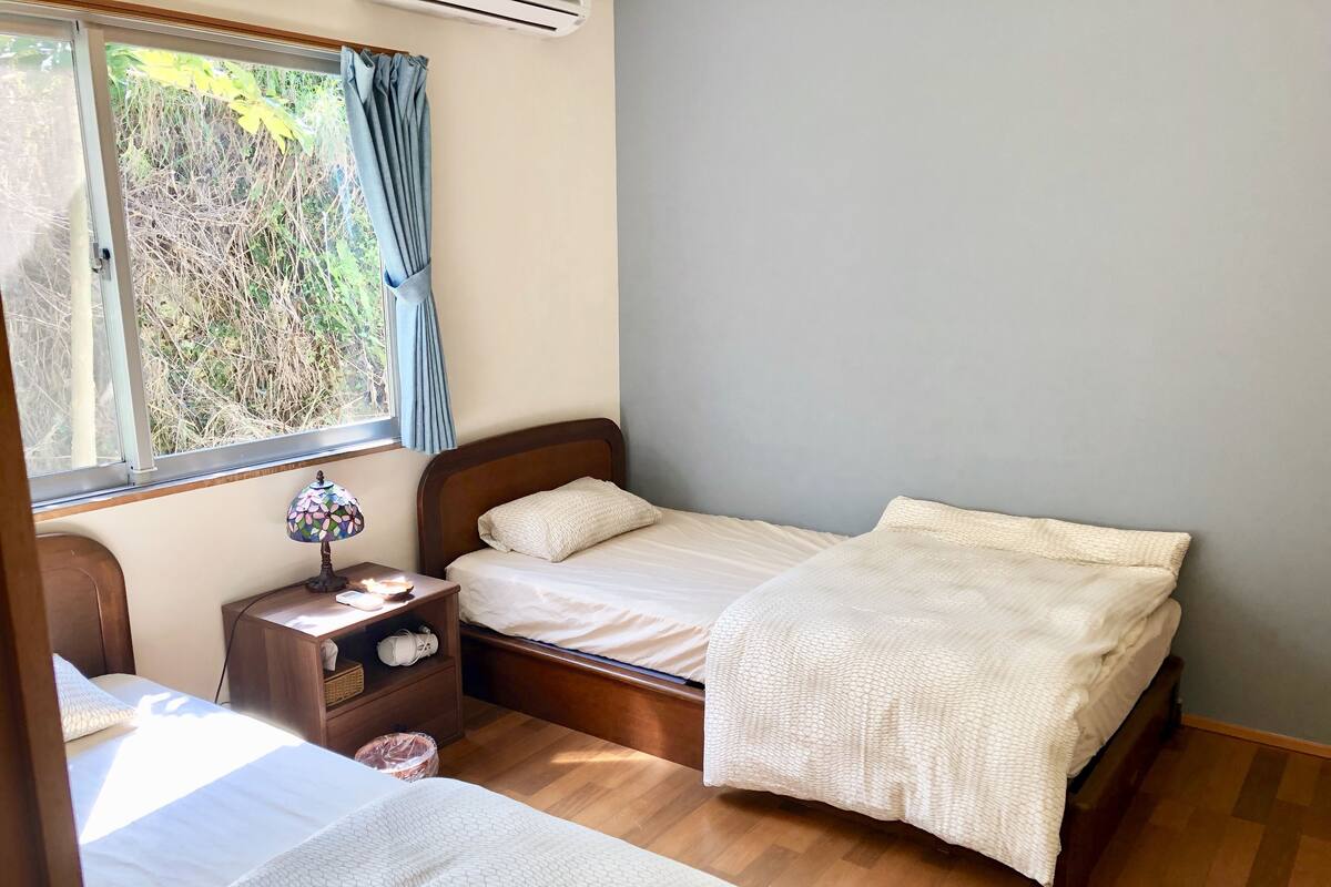Quarto com duas camas, mesa de cabeceira com abajur e janela com cortinas.