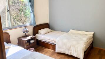 A bedroom with two beds, a nightstand with a lamp, and a window with curtains.