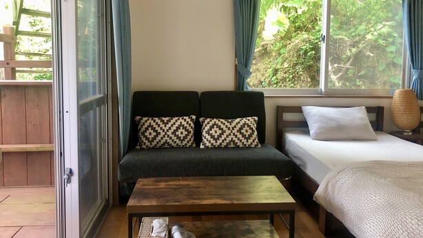 A room with a sofa, a bed, a table, and a window with curtains. - Life is a Journey - Hostel (Yomitan)