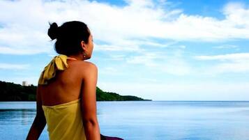 A person in a yellow garment overlooking a calm body of water with a distant landmass and a clear sky.