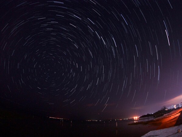 Une photographie de traînées d’étoiles avec un pont et des lumières au premier plan.
