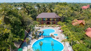 Un resort con una amplia piscina, palmeras y un edificio de techo rojo.