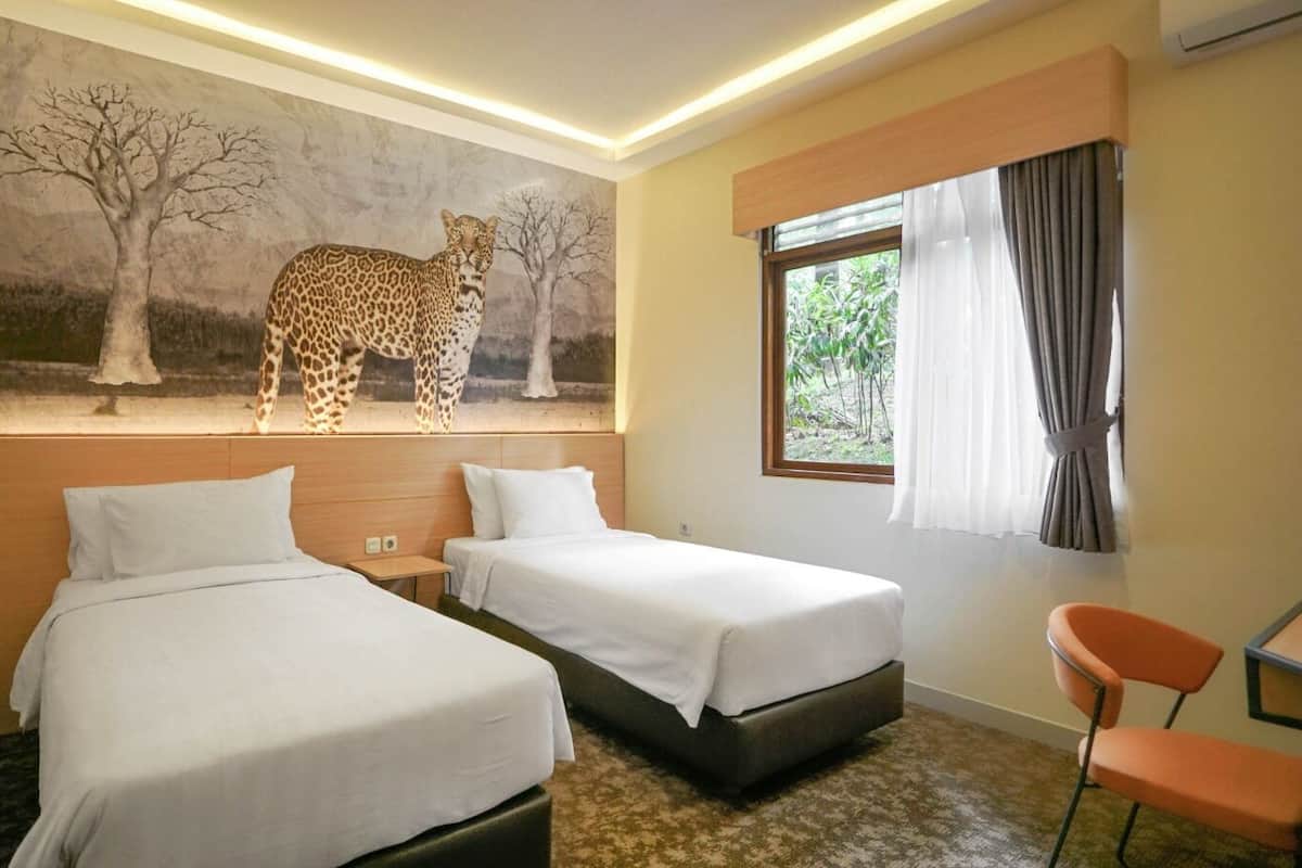 Une chambre d’hôtel avec deux lits, une fresque représentant un léopard et des girafes, une fenêtre avec des rideaux et une chaise.