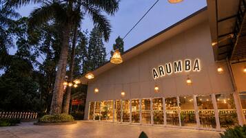 A building with the name 'ARUMBA' illuminated on the facade, surrounded by trees and outdoor seating.