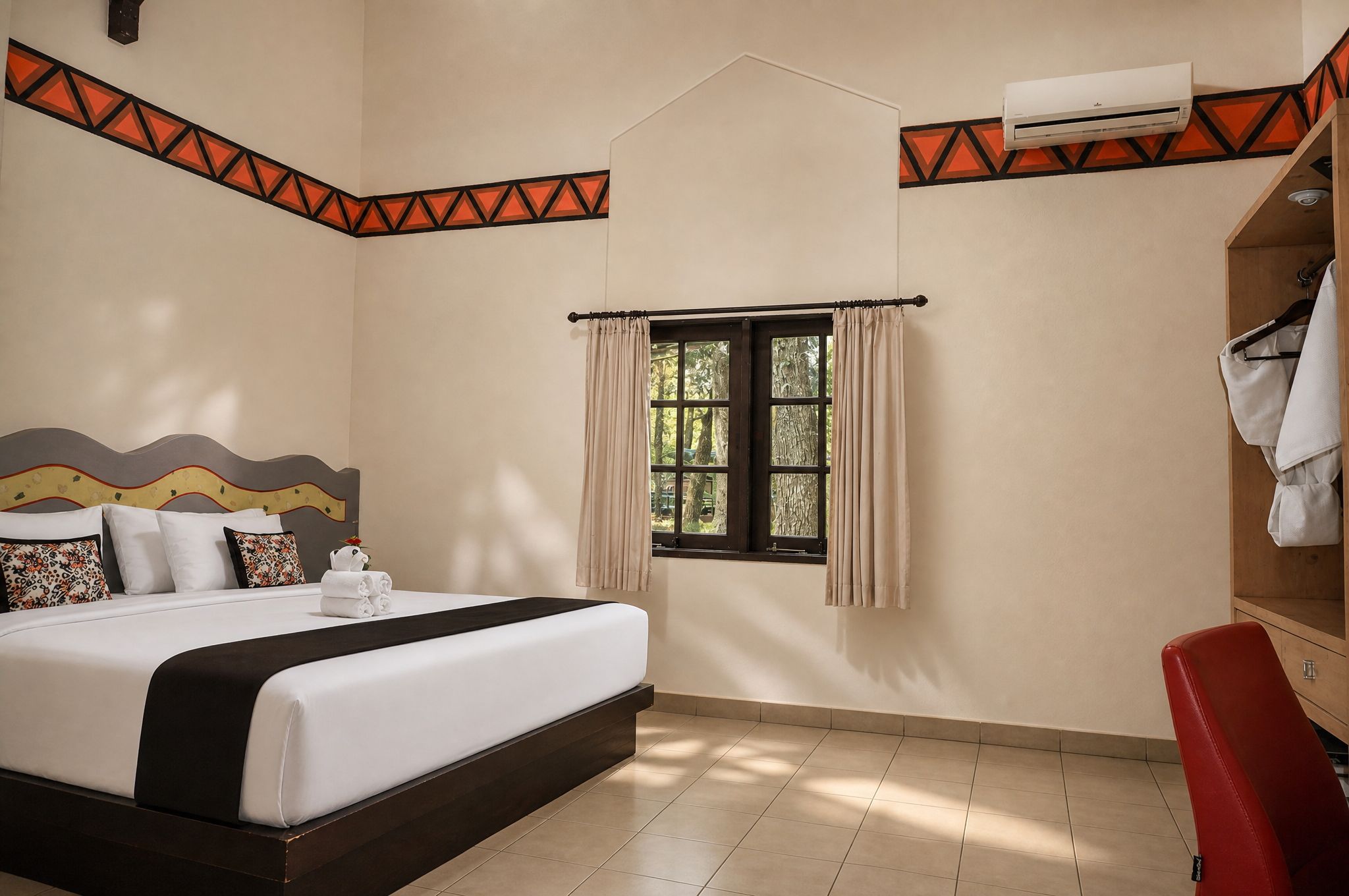 A hotel room with a bed, a window with curtains, a red chair, and an air conditioning unit.