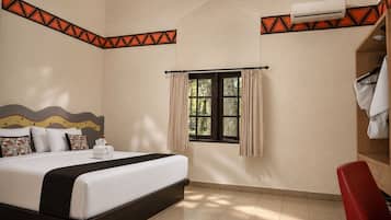 A hotel room with a bed, a window with curtains, a red chair, and an air conditioning unit.