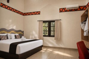 Une chambre d’hôtel avec un lit, une fenêtre avec des rideaux, une chaise rouge et un appareil de climatisation.