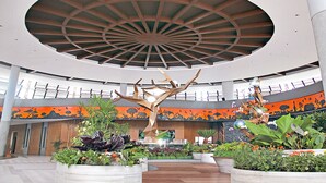 A spacious atrium with a high ceiling, a central tree sculpture, and a variety of indoor plants.