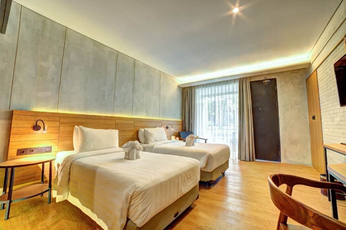 Une chambre d’hôtel avec deux lits, une tête de lit en bois, une petite table, une chaise et un téléviseur fixé au mur.