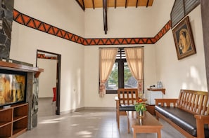 A living room with a fireplace, a television, a sofa, a coffee table, and a window with curtains. - Royal Safari Garden Resort & Convention (Cisarua)