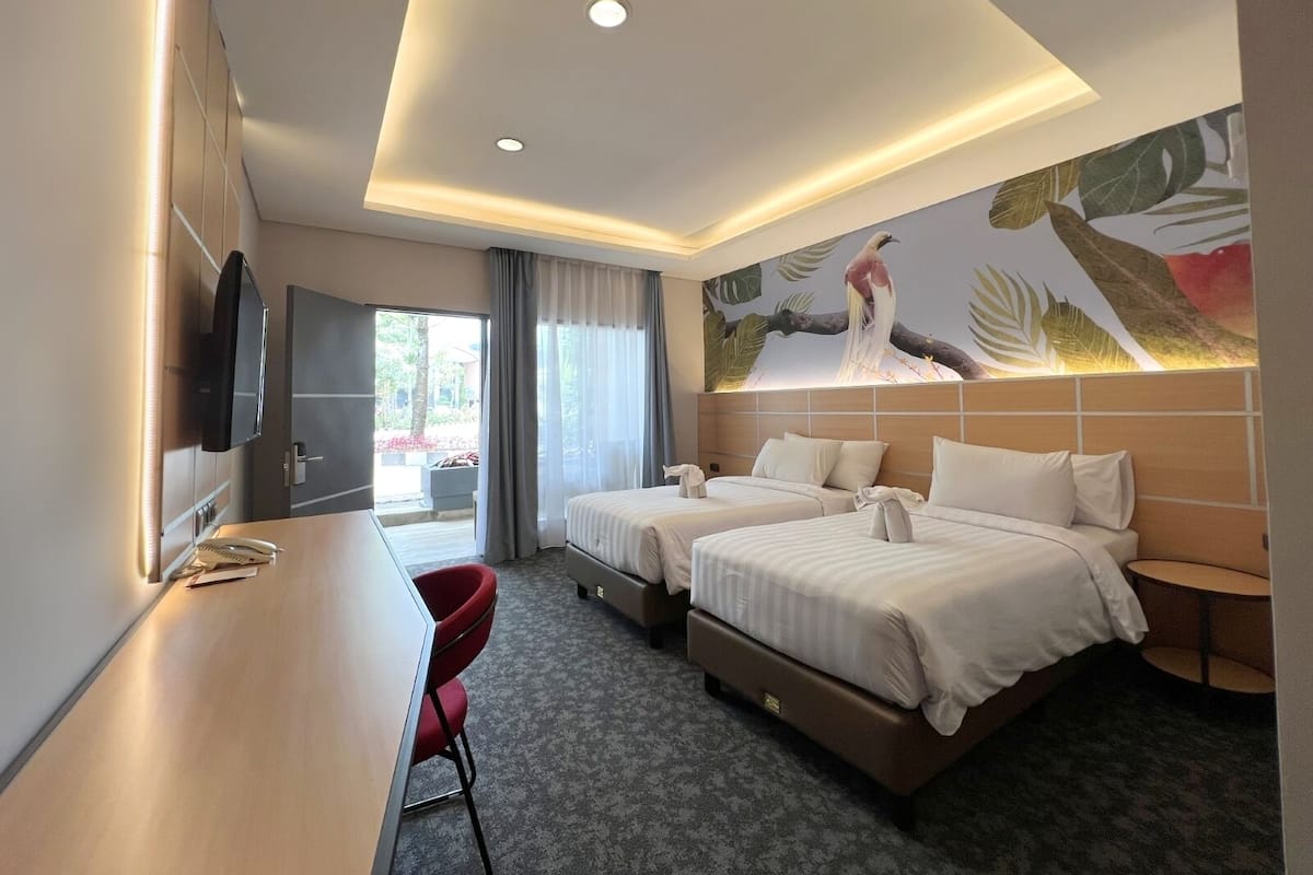Une chambre d’hôtel avec deux lits, un bureau, une télévision et une fresque représentant un oiseau.