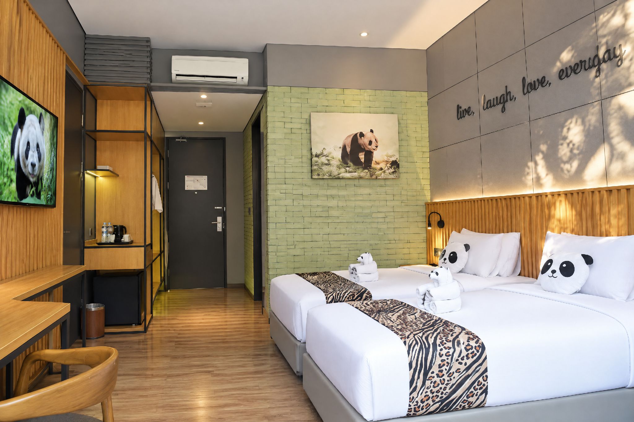 A hotel room with a bed, a desk, a TV, and a panda-themed wall decoration.
