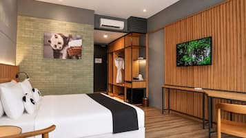 A modern hotel room with a bed, a desk, a TV, and a panda-themed artwork.