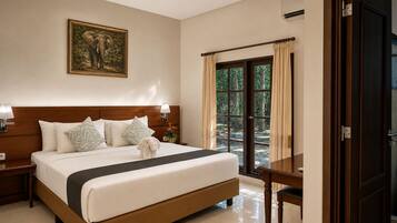 A hotel room with a large bed, a nightstand, a lamp, a painting of an elephant, and a view of the outdoors through a door.