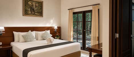 A hotel room with a large bed, a nightstand, a lamp, a painting of an elephant, and a view of the outdoors through a door.
