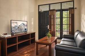 A living room with a television, a sofa, a coffee table, and a window with curtains. - Royal Safari Garden Resort & Convention (Cisarua)