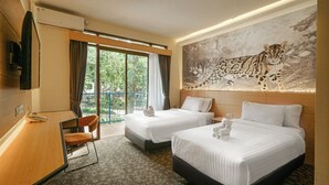 A hotel room with two beds, a desk, a chair, and a large window with a view of greenery.
