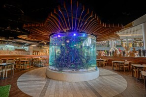 A restaurant with a central aquarium, wooden ceiling, and dining area with tables and chairs. - Royal Safari Garden Resort & Convention (Cisarua)