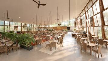 A spacious indoor dining area with multiple tables and chairs, large windows, and hanging light fixtures.