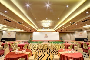 Een feestzaal met ronde tafels, stoelen en een podium met een presentatiescherm.