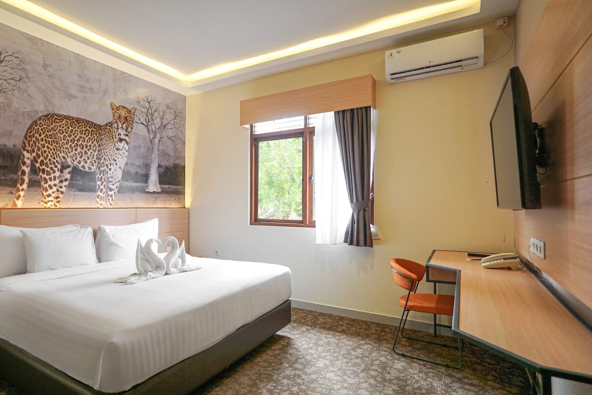 Une chambre d’hôtel avec un grand lit, un bureau, une chaise, un téléviseur fixé au mur, un appareil de climatisation et une fresque représentant un léopard sur le mur.