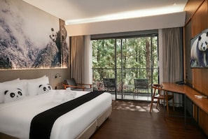 A hotel room with a bed, a desk, a chair, and a balcony with a view of trees. - Royal Safari Garden Resort & Convention (Cisarua)
