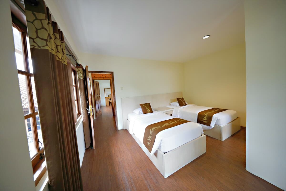 Une chambre d’hôtel avec deux lits, un plancher en bois et une vue par la fenêtre, qui est dotée de rideaux.