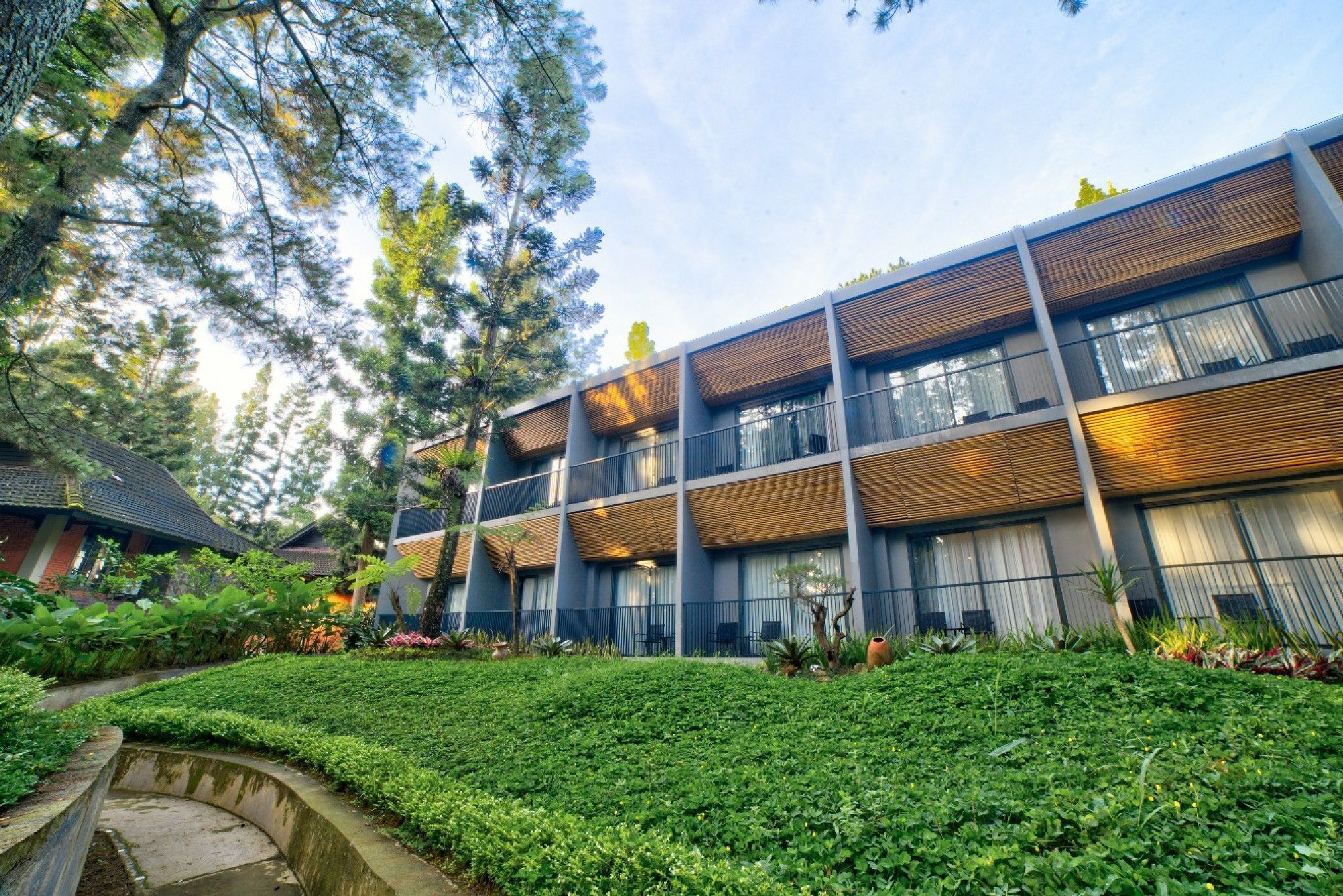 A modern building with multiple balconies, surrounded by lush greenery and a well-maintained garden.
