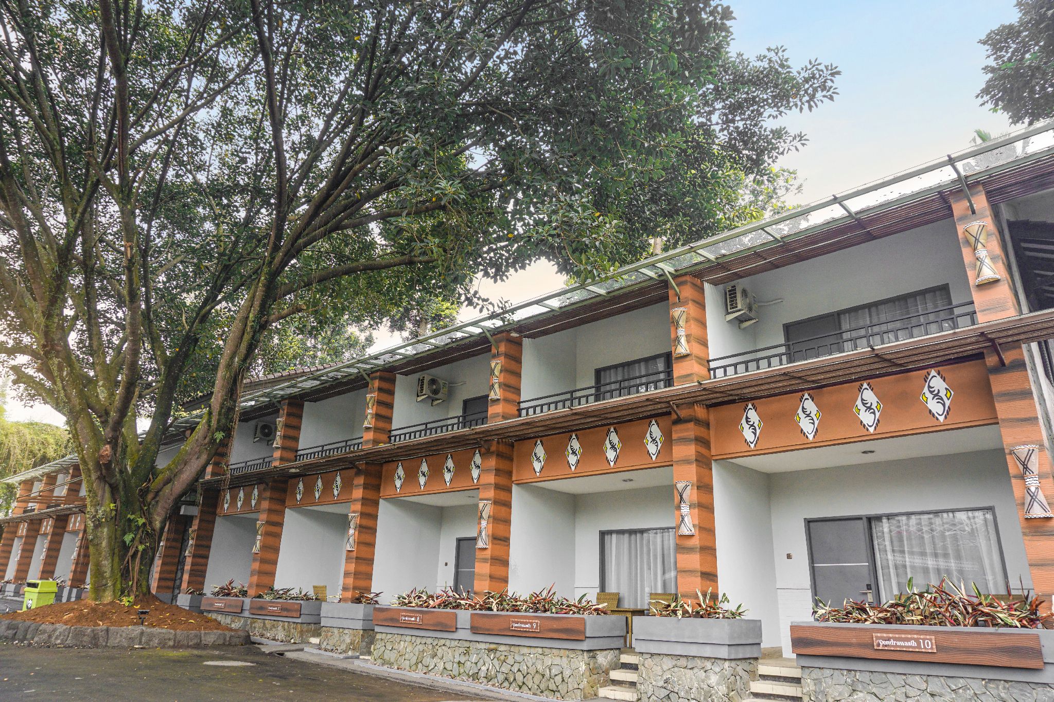 A multi-story hotel with a traditional architectural style, featuring a balcony on each floor and a large tree in front.