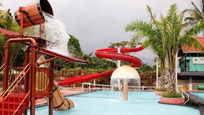 A water park with a red slide, a water fountain, and a pool.