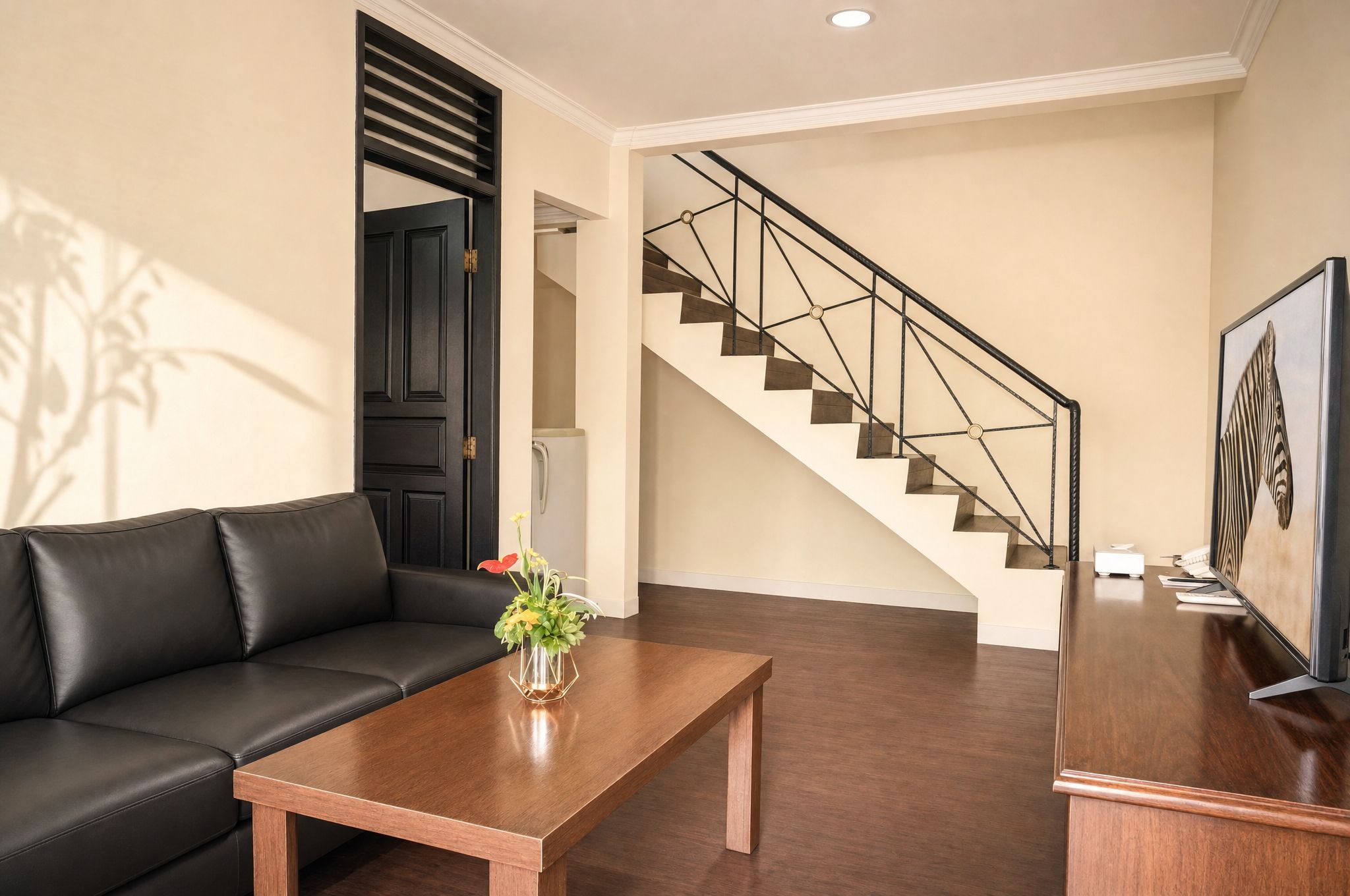 A modern living room with a black leather sofa, a wooden coffee table, and a staircase with a metal railing.