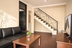 A modern living room with a black leather sofa, a wooden coffee table, and a staircase with a metal railing. - Royal Safari Garden Resort & Convention (Cisarua)
