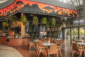 A restaurant with a curved wall mural, hanging plants, and a variety of seating arrangements.