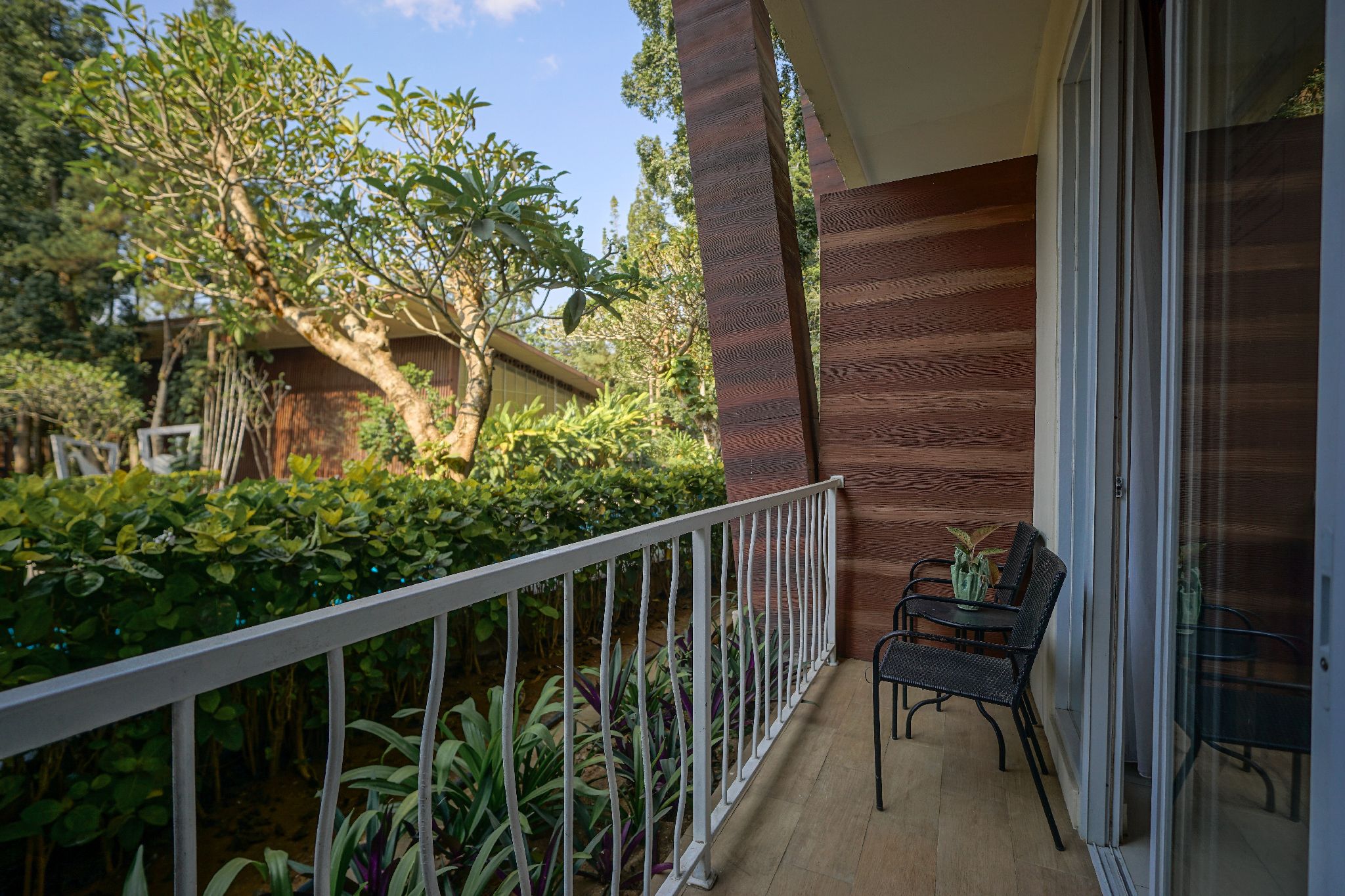 Un balcon avec une balustrade blanche, une petite table avec deux chaises et un pot de fleurs.