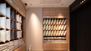 A neatly organized storage area with shelves of folded towels and linens, a small trash bin, and a wall-mounted security camera. - Super Hotel Shinagawa Aomonoyokocho (Tokyo)