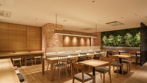 A modern restaurant with wooden tables and chairs, a brick accent wall, and a green wall with foliage. - Super Hotel Shinagawa Aomonoyokocho (Tokyo)
