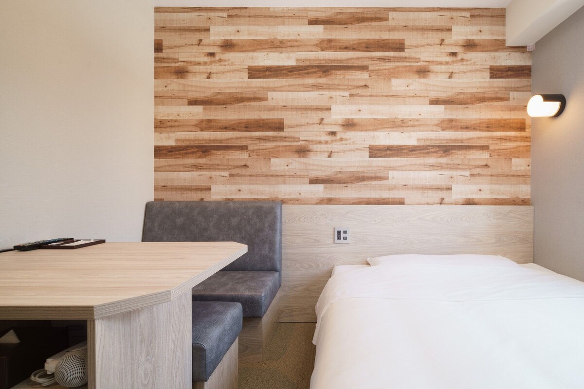 A hotel room with a wooden wall panel, a bed, a gray sofa, and a small table.