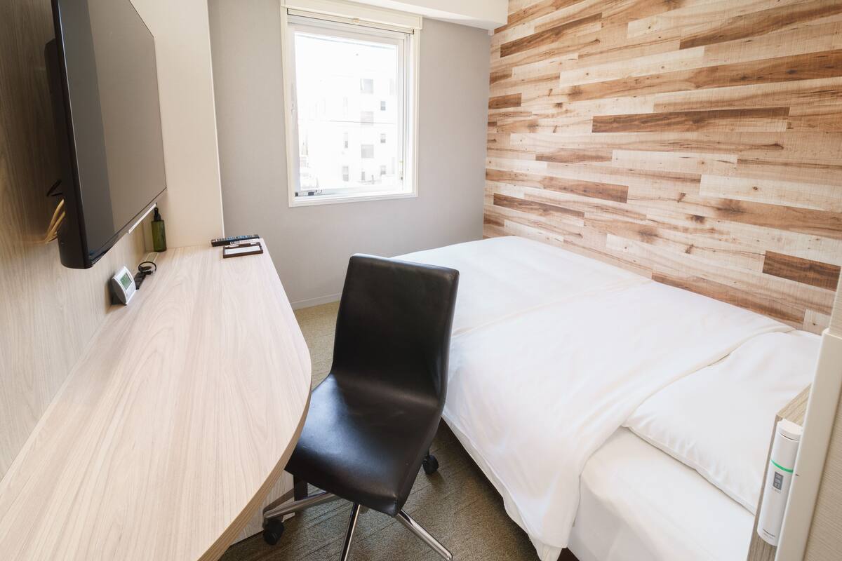 A hotel room with a wooden wall, a bed, a desk, and a chair.