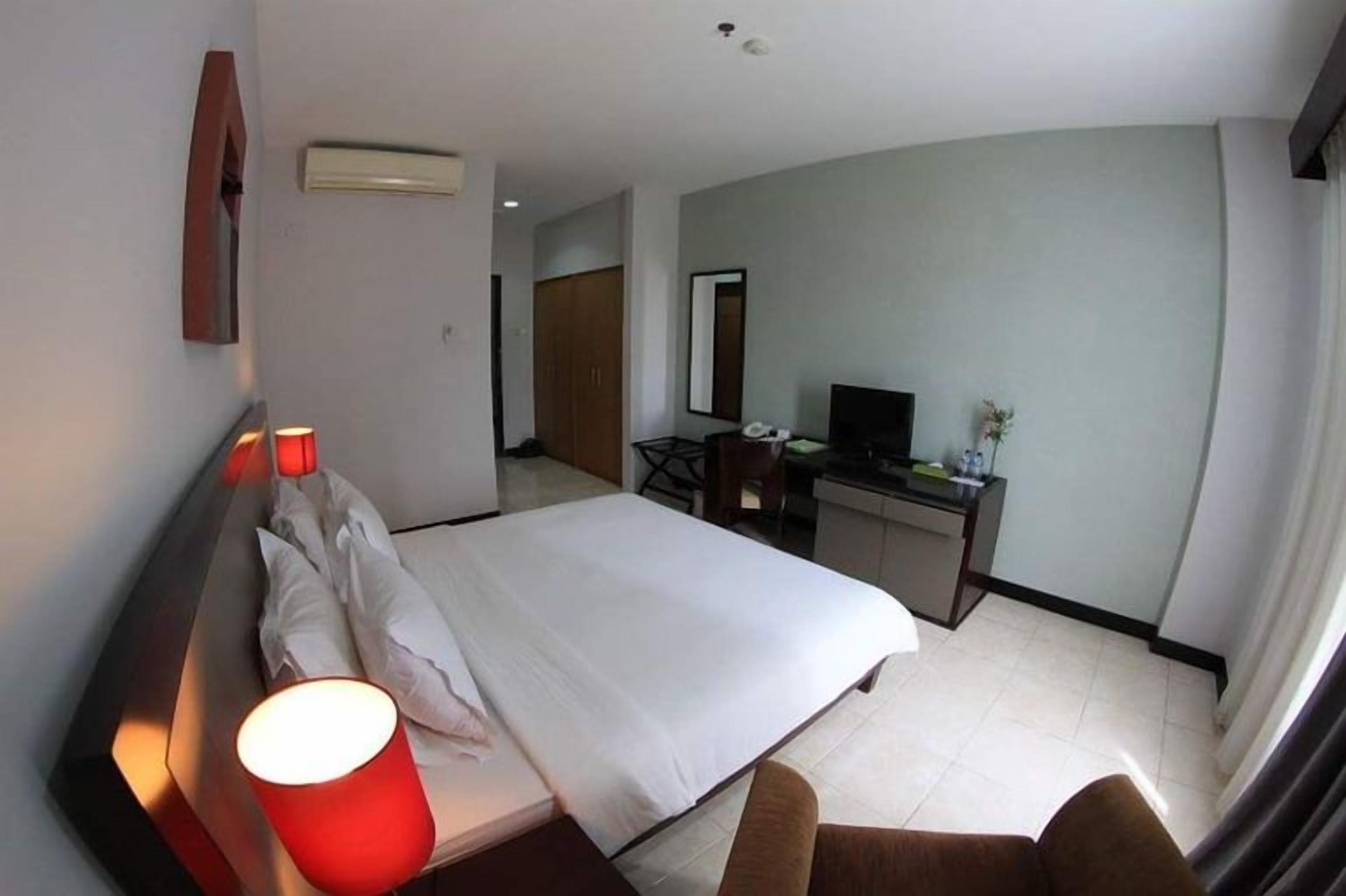 A hotel room with a bed, a desk, a chair, a TV, and a lamp.