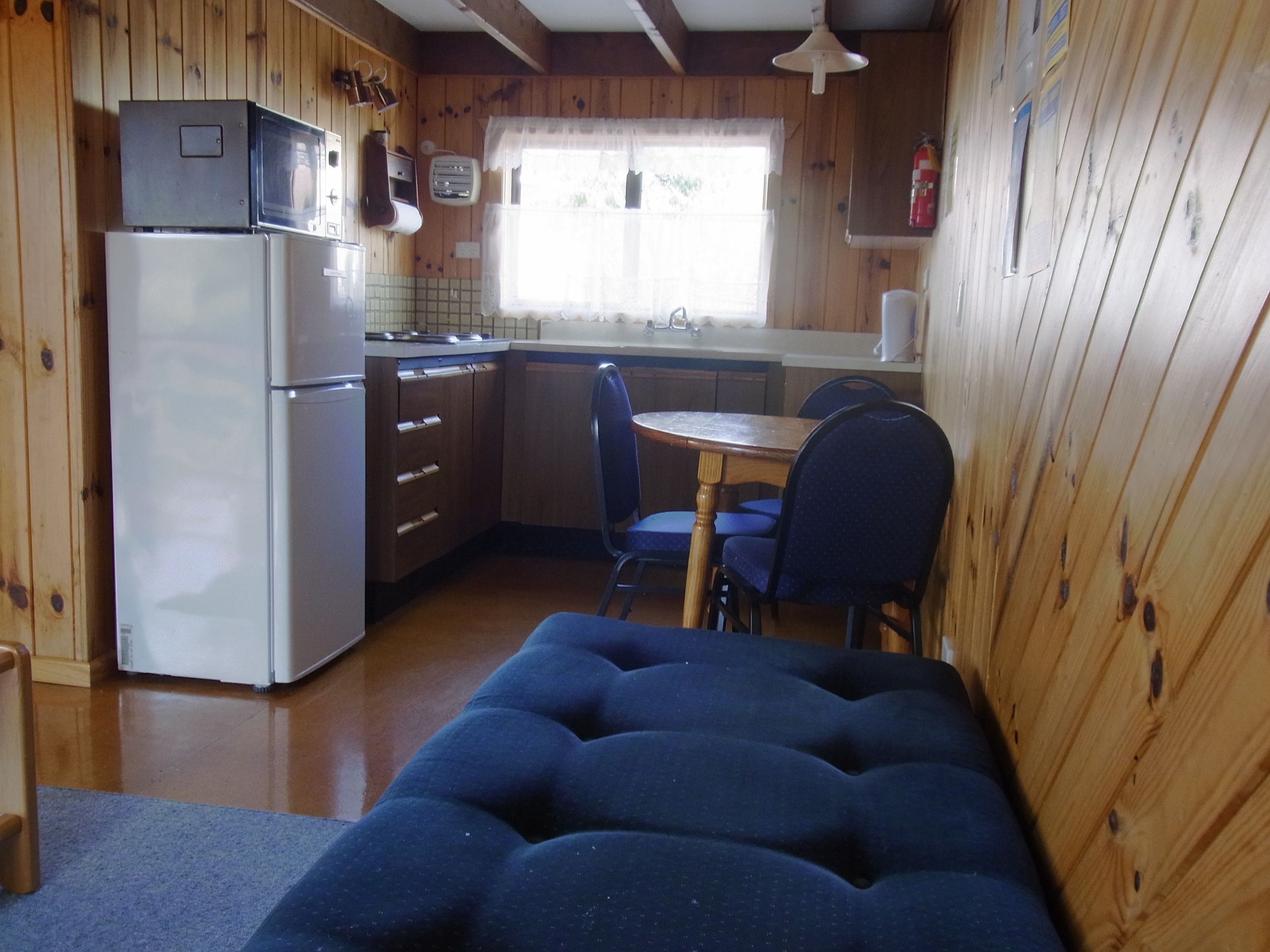 Une cuisine compacte équipée d’un réfrigérateur, d’une cuisinière et d’un évier. On y trouve une table à manger avec des chaises et un banc bleu avec un coussin.