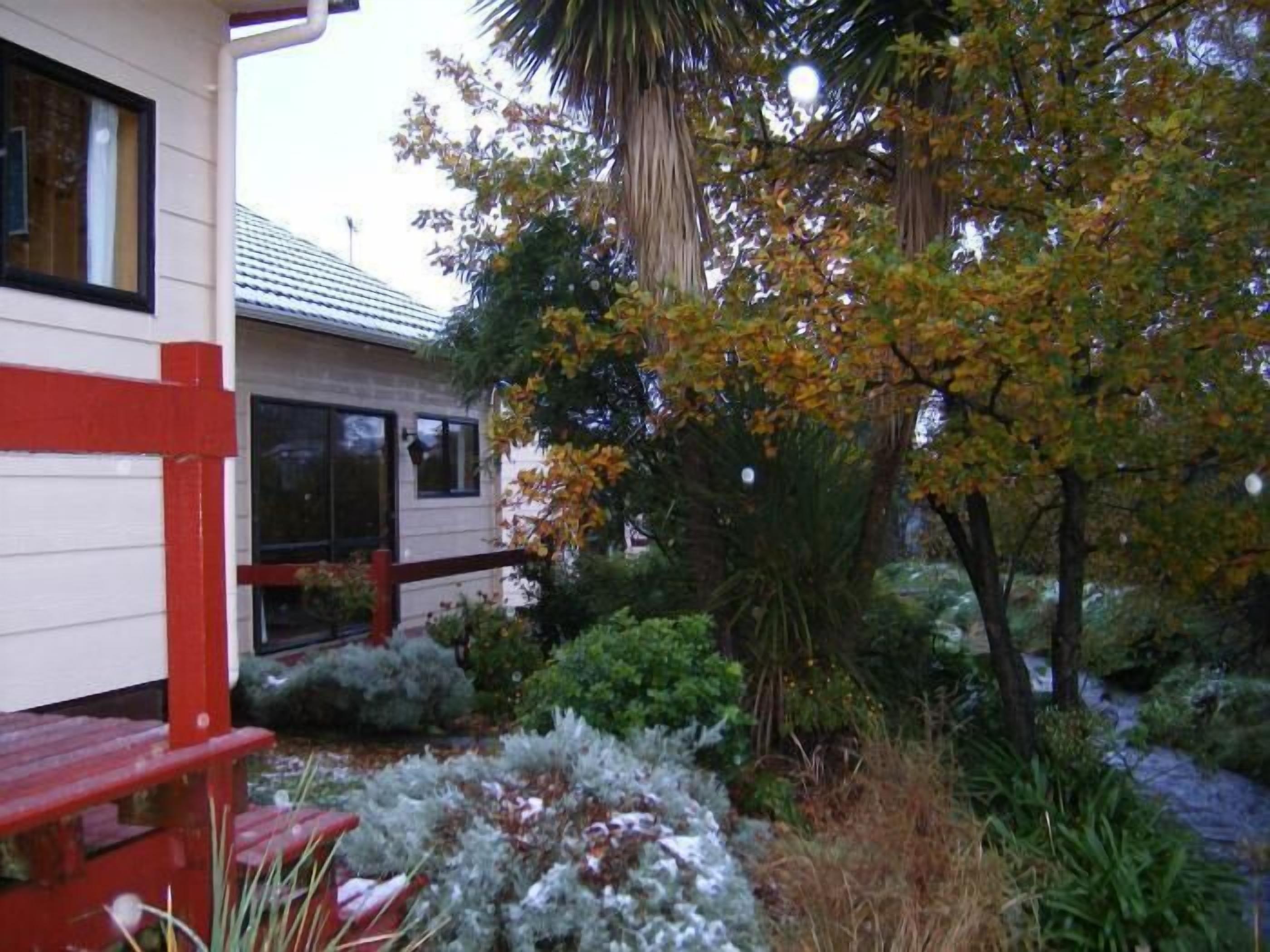 A house with a red deck, a covered porch, and a garden with various plants and trees.