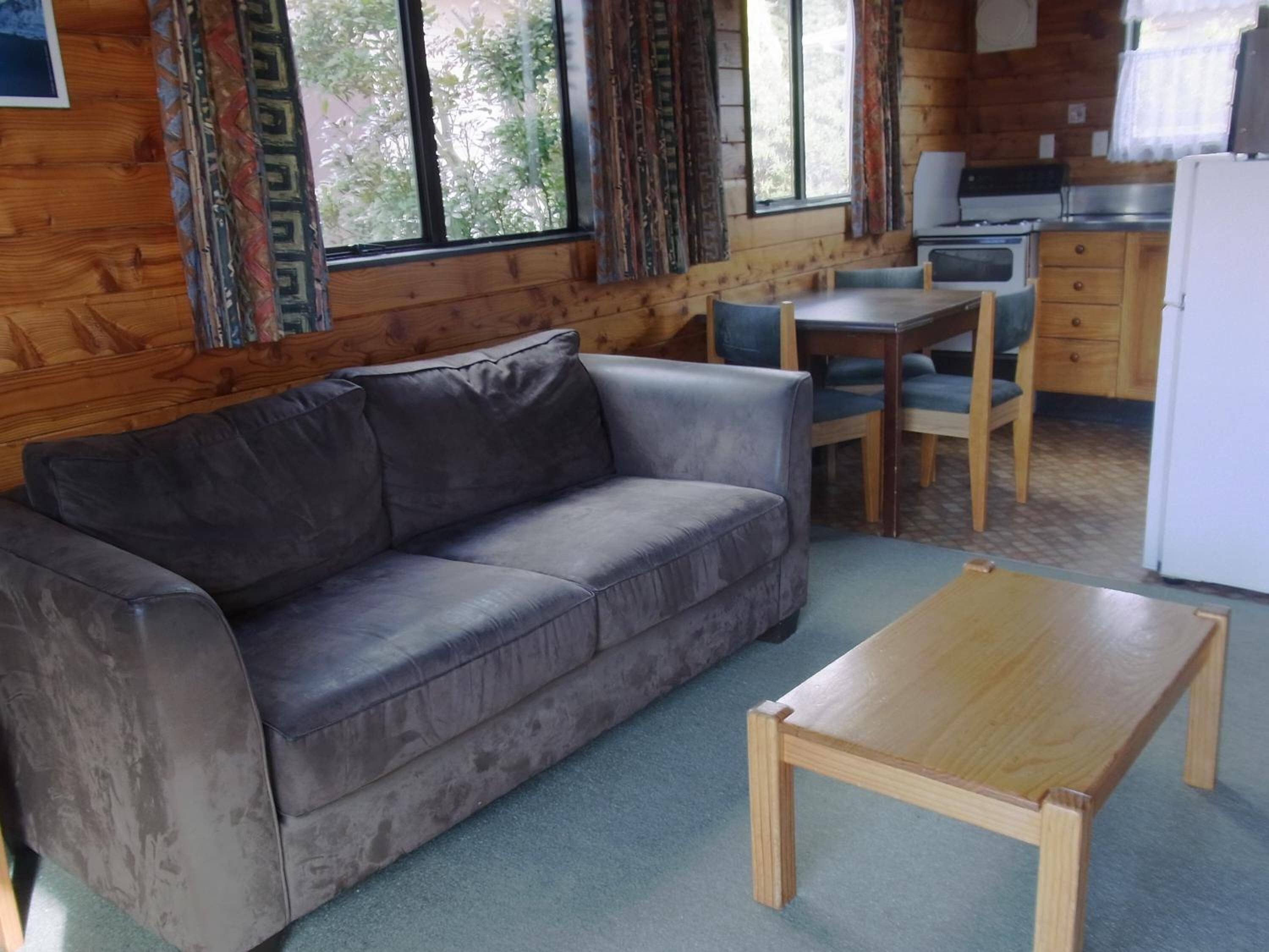 A cozy room with a gray sofa, a wooden coffee table, and a kitchen area with a refrigerator, stove, and cabinets.