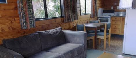 A cozy room with a gray sofa, a wooden coffee table, and a kitchen area with a refrigerator, stove, and cabinets.